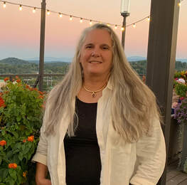 Laura Andrews, middle-aged woman standing on rrooftop in Knoxville at sunset with Smokey mountains in the background. 