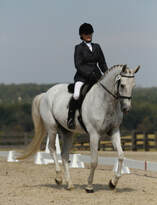 Laura Andrews riding english-style in sport of dressage on grey horse in arena with low white rails. 